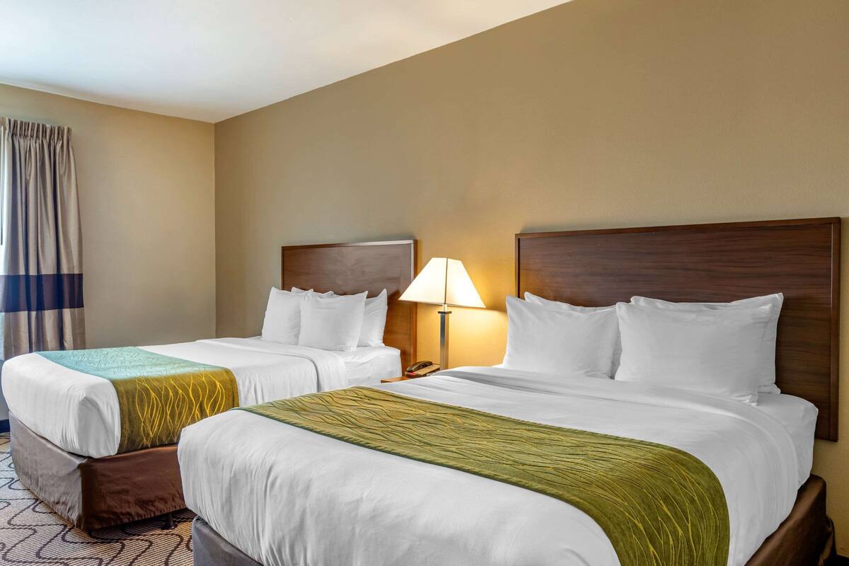 Una camera d'albergo con due letti, un comodino con una lampada e una tenda alla finestra.