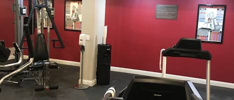 Ein Fitnessstudio mit Laufbändern, Kraftgeräten und einer roten Wand mit Trainingspostern.