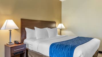 A hotel room with a large bed, two bedside lamps, a nightstand with a phone, and a blue accent on the bedspread.