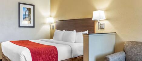 A hotel room with a large bed, two bedside lamps, a framed picture on the wall, and a gray armchair.