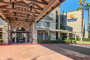 A hotel entrance with a stone facade, a covered walkway, and a clear sky. - Comfort Inn & Suites Orange County John Wayne Airport (Santa Ana)