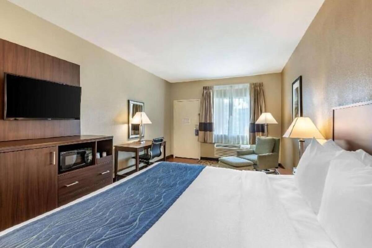 Una camera d'albergo con un letto, una scrivania, una TV e una finestra con tende.