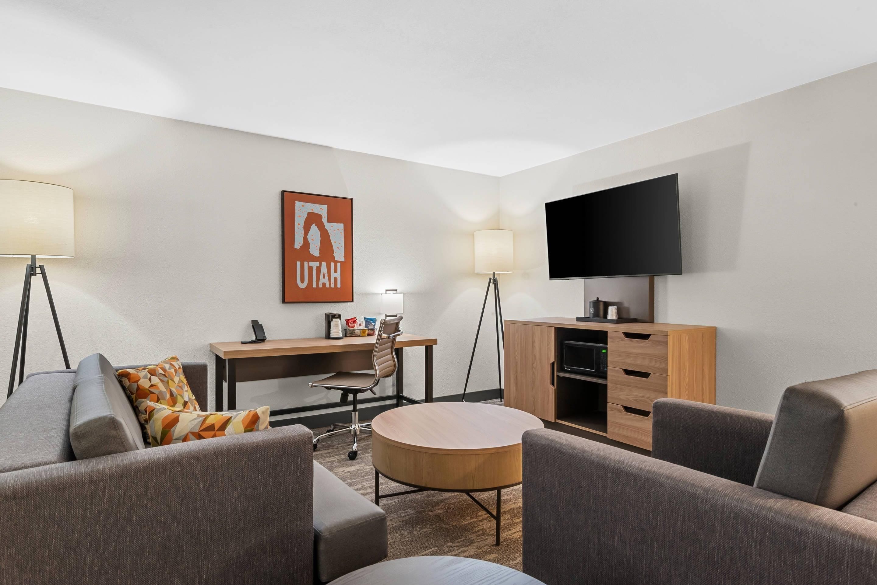A hotel room with a flat-screen TV, a desk, two chairs, a sofa, and a coffee machine.