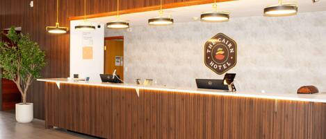 A reception desk with a wooden finish, overhead lighting, and a logo for 'The Cairn Hotel' on the wall.