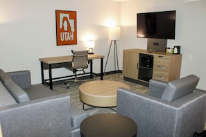 Une chambre d’hôtel comprenant un canapé, une table basse ronde, un bureau avec une chaise, une télévision, une lampe et une kitchenette.
