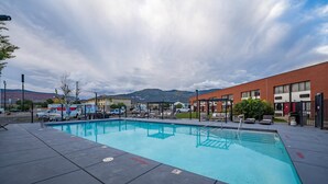 A swimming pool with a tiled deck, a brick building in the background, and mountains in the distance. - The Cairn Hotel, an Ascend Collection Hotel (Cedar City)
