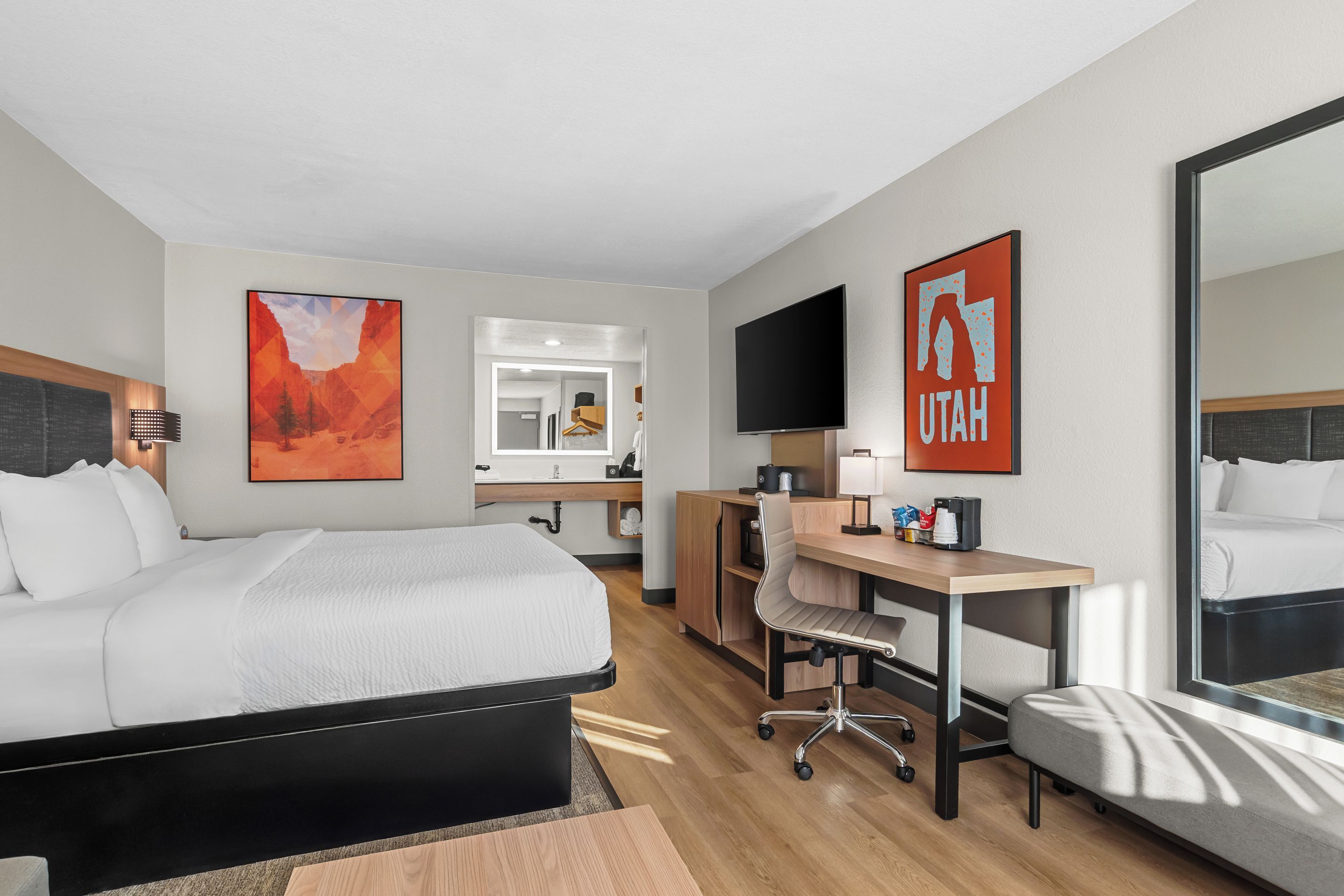 Une chambre d’hôtel avec un lit, un bureau, une chaise et un grand miroir.