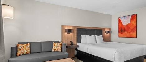 Una habitación de hotel con sofá, cama, mesita de noche, lámpara y un cuadro en la pared.