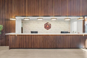 Un comptoir d’accueil avec un panneau en bois en arrière-plan, un logo sur le mur et un éclairage suspendu au plafond.