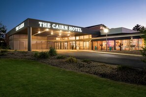 L’extérieur de l’hôtel The Cairn, avec son entrée bien éclairée et son parterre aménagé.