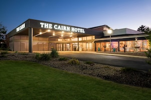 Exterior del Hotel Cairn, con una entrada bien iluminada y un jardín frontal ajardinado.
