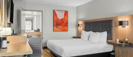 Une chambre d’hôtel avec un lit, un bureau, une chaise et un tableau au mur.