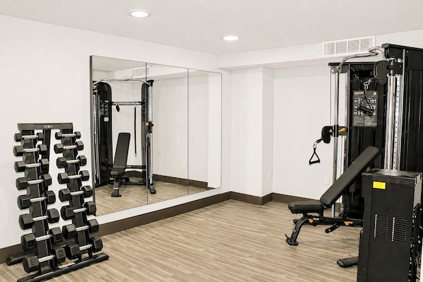 Une salle de sport équipée de miroirs, de supports pour les poids et d'appareils d'exercice.