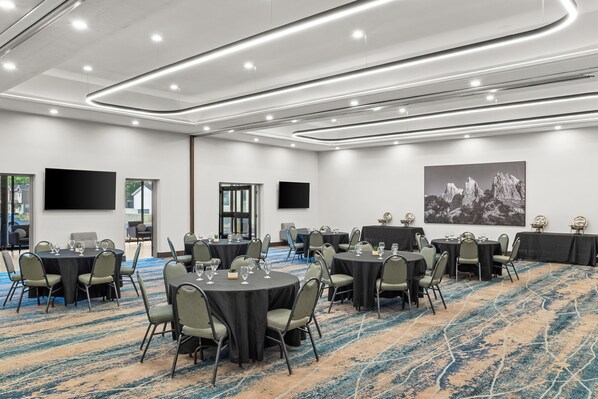 Une salle de conférence dotée de plusieurs tables et chaises, d’un grand tableau accroché au mur et d’un sol recouvert de moquette.