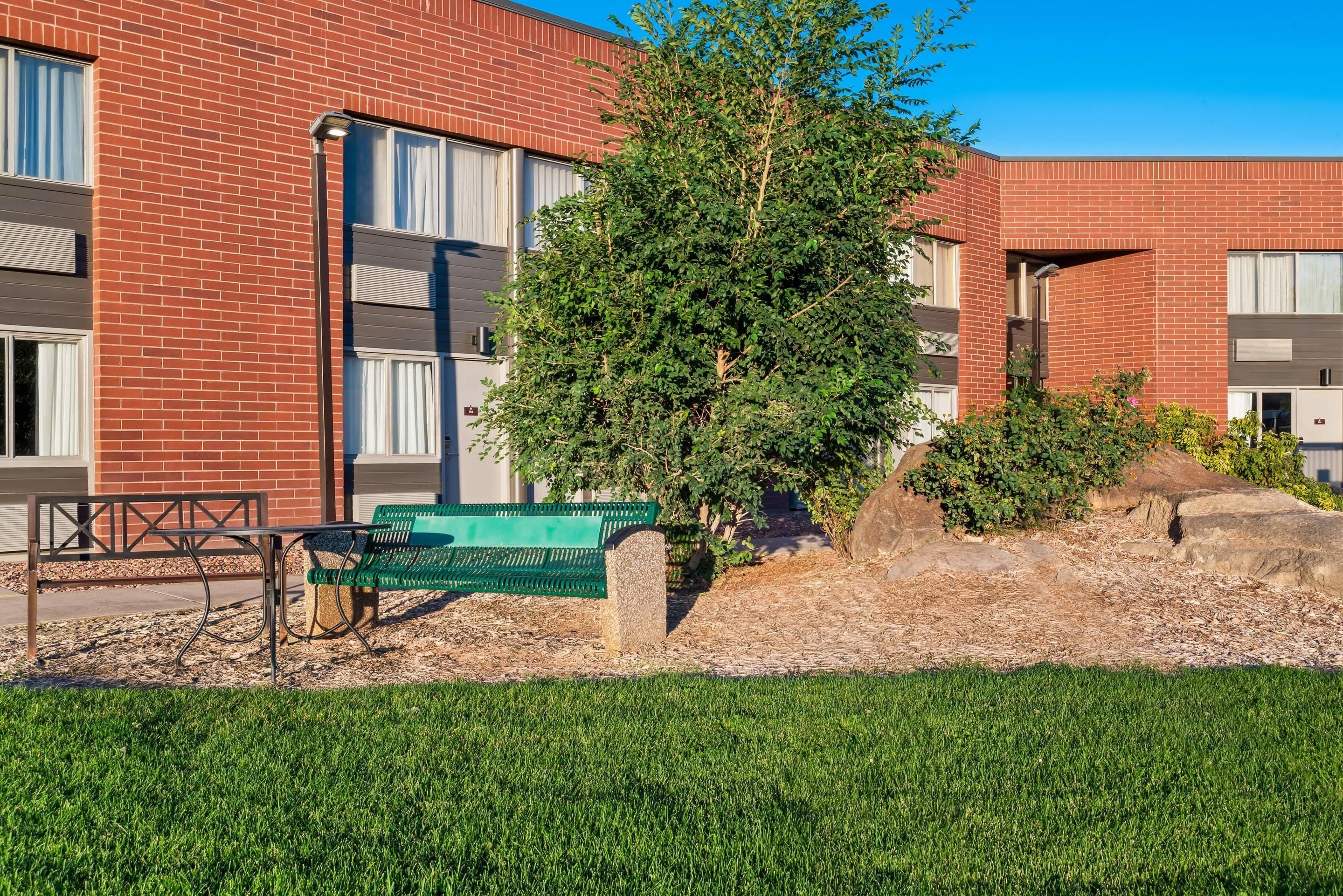 A building with red brick walls, a green bench, and a tree in front.