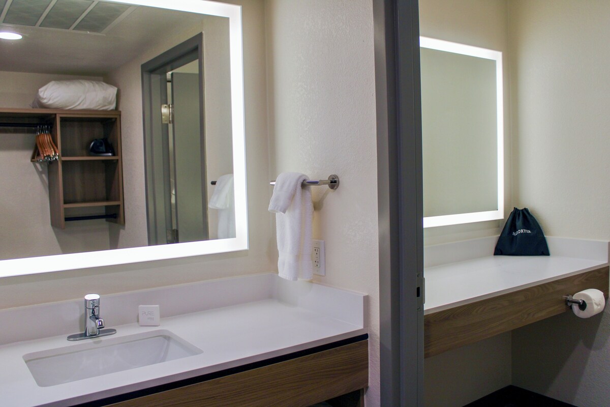 Une salle de bain avec un lavabo blanc, un miroir, un porte-serviettes et une étagère en bois.