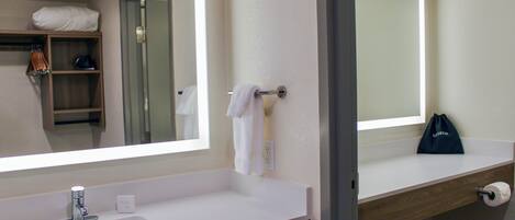 Un baño con lavamanos blanco, espejo, toallero y repisa de madera.