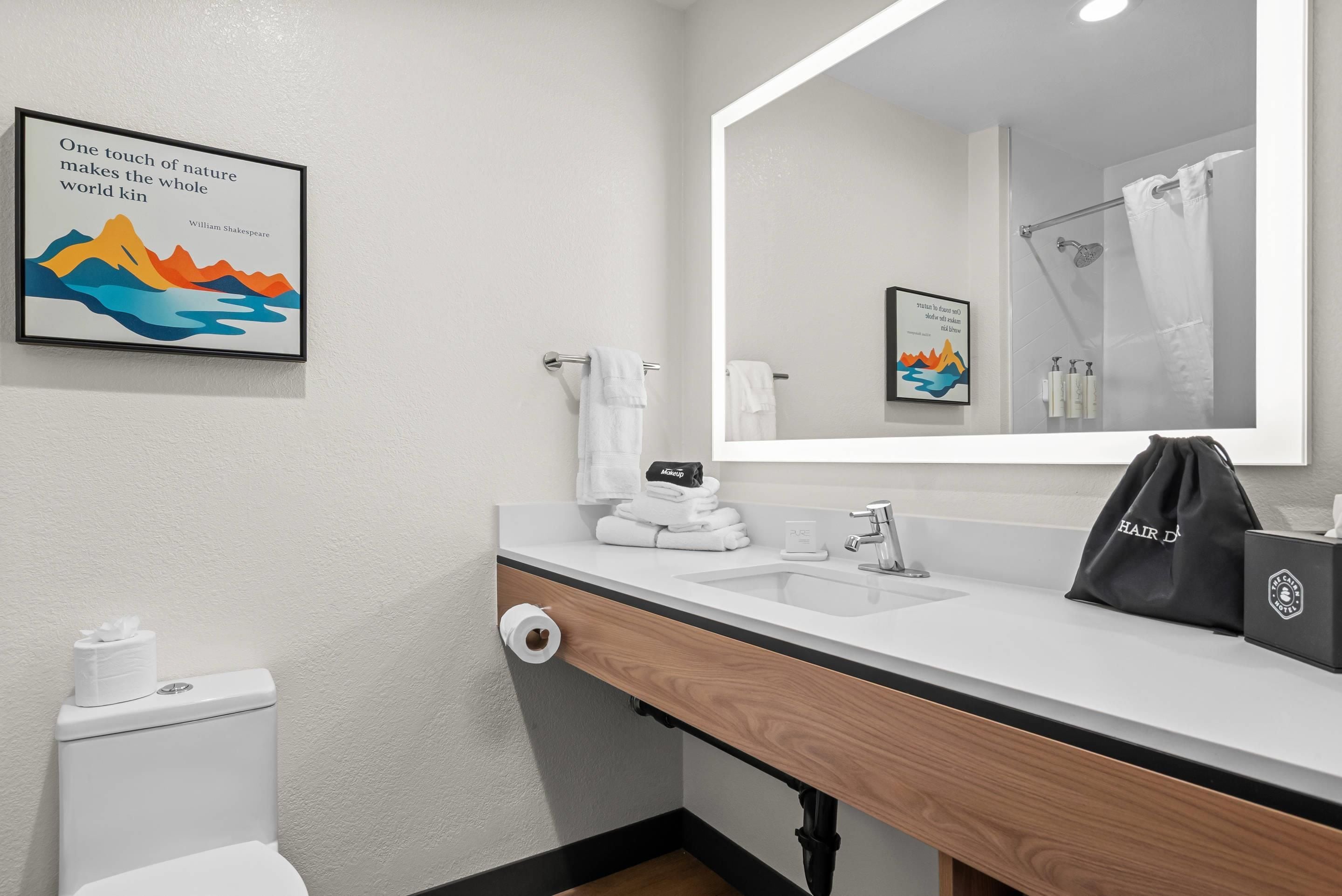 Une salle de bain moderne avec un lavabo blanc, un miroir, des toilettes et un porte-serviettes. Deux citations encadrées ornent le mur.