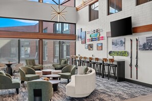 Een moderne loungehoek met zitplaatsen, een wandgemonteerde televisie en ski's aan de muur.
