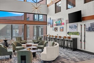 A modern lounge area with seating, a mounted TV, and ski equipment on the wall.