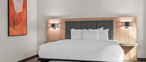 A modern hotel room with a large bed, a headboard with built-in lighting, a bench at the foot of the bed, and a painting on the wall.