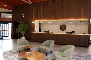Een receptiegedeelte met een houten receptiebalie, twee fauteuils, een bijzettafeltje en een potplant.