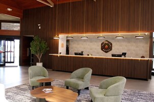 Uma área de recepção com balcão de madeira, duas poltronas, uma mesa de centro e um vaso de planta.