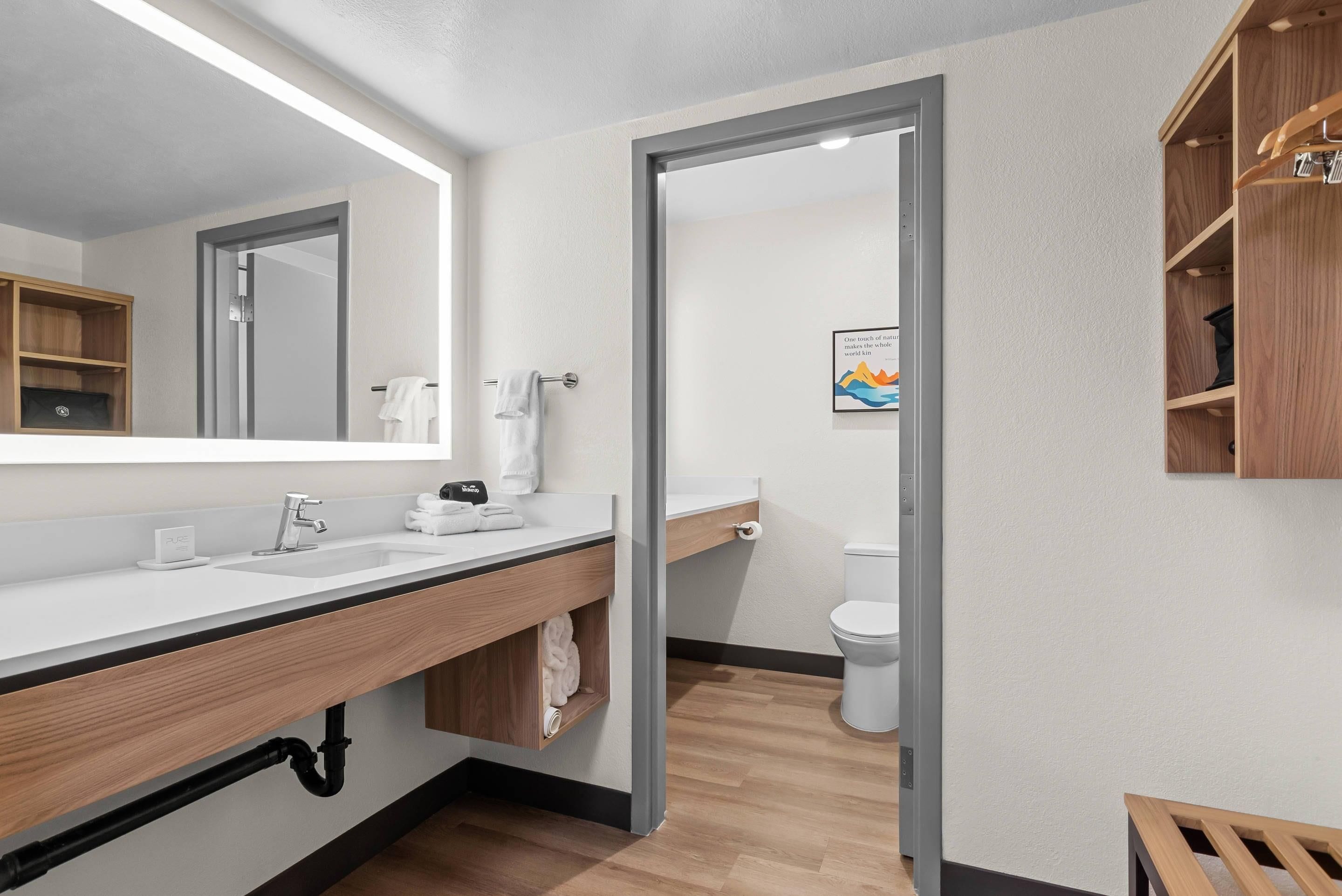 Et moderne badeværelse med et stort spejl, en vask, et toilet og en hylde i træ.