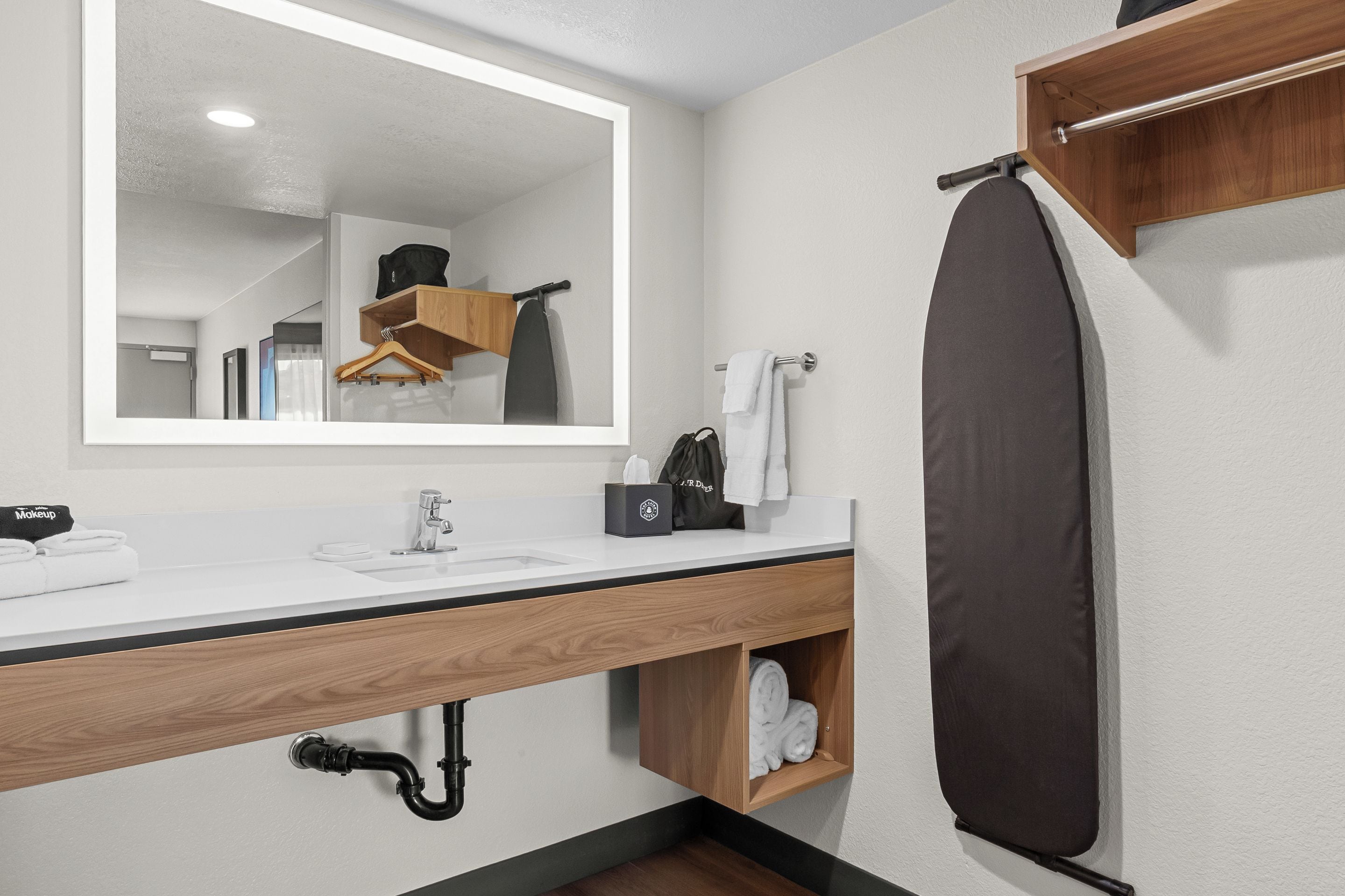 Un baño moderno con un espejo grande, un lavamanos con toallero, una cortina de ducha colgante y un estante de madera con toallas.