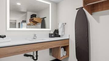 Un baño moderno con un espejo grande, un lavamanos con toallero, una cortina de ducha colgante y un estante de madera con toallas.