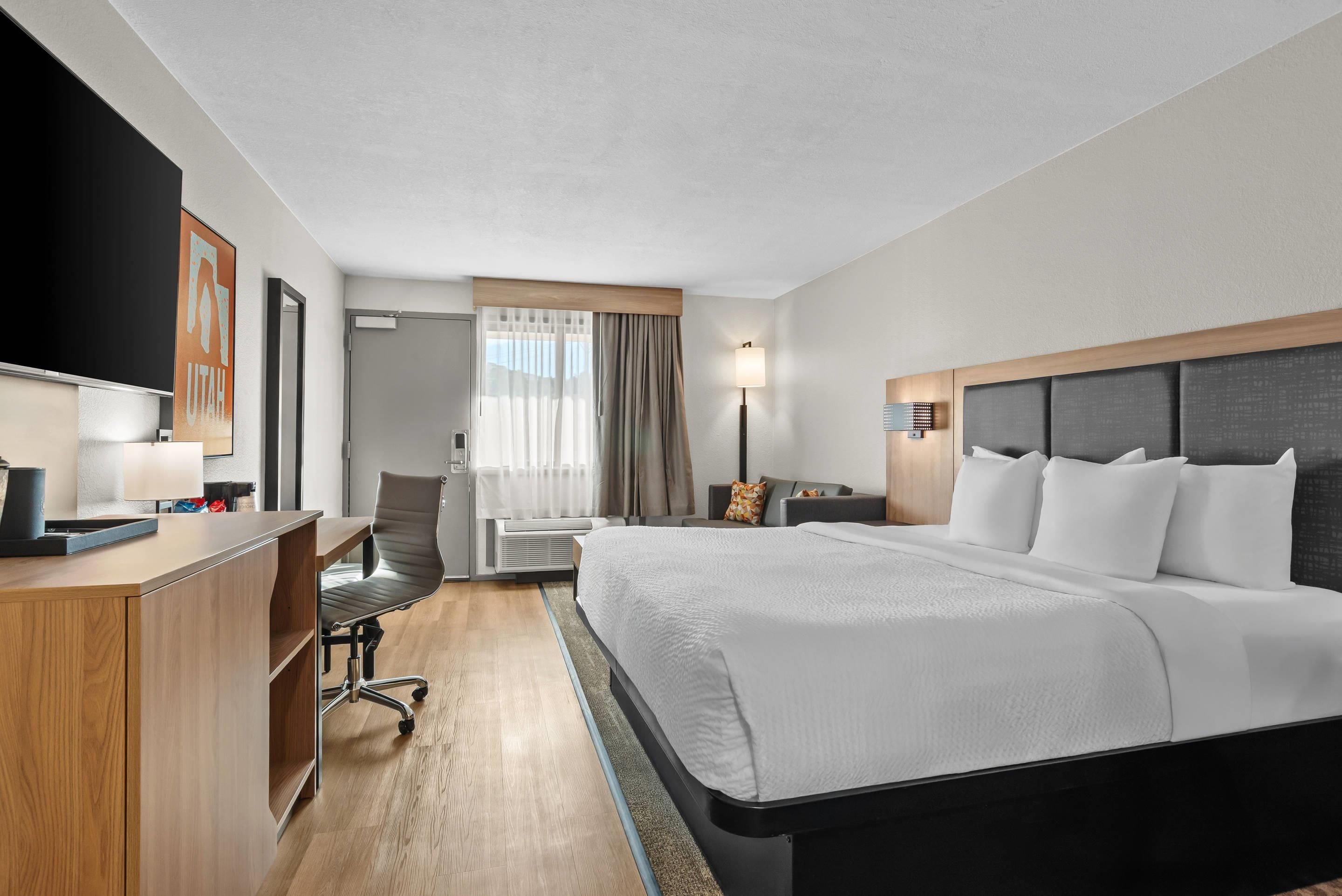 A hotel room with a bed, desk, chair, and a television.