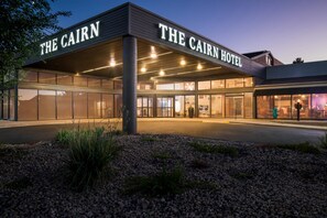 The Cairn Hotel with a modern facade, large glass windows, and a well-lit entrance.