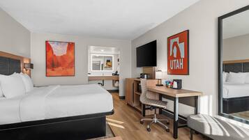 Habitación de hotel con cama, escritorio, silla y un espejo grande.