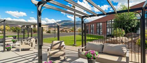 Un espacio de estar al aire libre cubierto con una pérgola, mobiliario exterior y plantas en macetas.