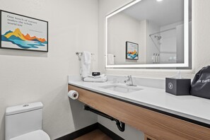 Une salle de bain moderne avec un grand miroir, un lavabo, des toilettes et une douche. On trouve des serviettes et des articles de toilette sur le comptoir.
