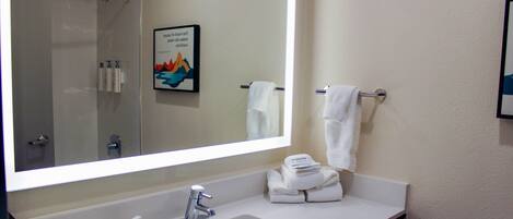 Une salle de bain avec un grand miroir, un lavabo, une douche et un porte-serviettes.