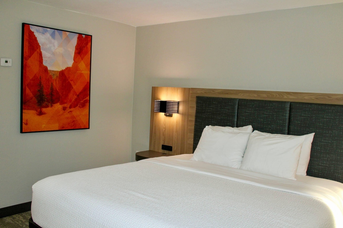 Une chambre d’hôtel avec un grand lit, une table de chevet, une lampe fixée au mur et un tableau.