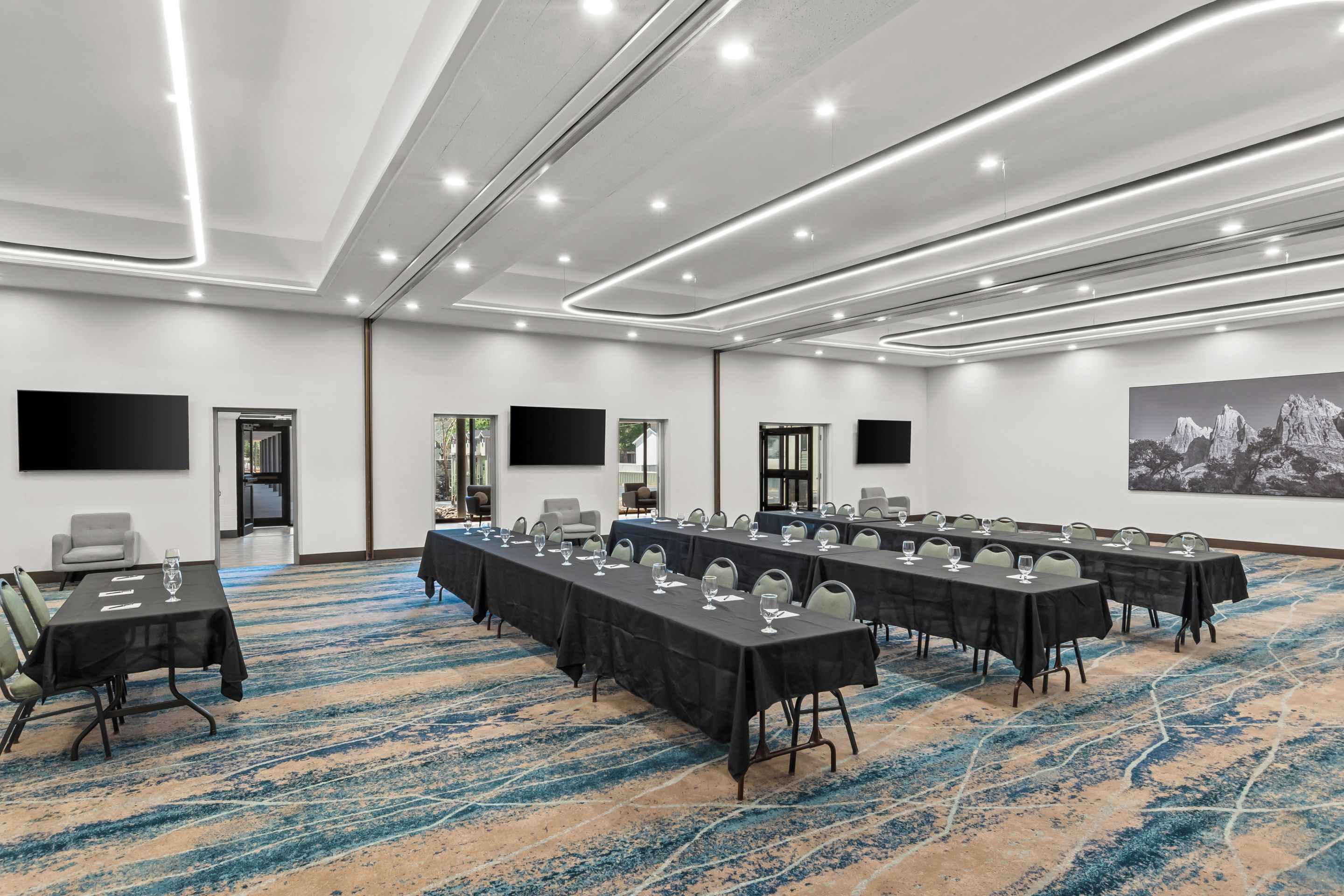 Un salón de conferencias con varias mesas, sillas y una pantalla grande.