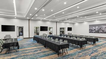 Un salón de conferencias con varias mesas, sillas y una pantalla grande.