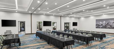 Un salón de conferencias con varias mesas, sillas y una pantalla grande.