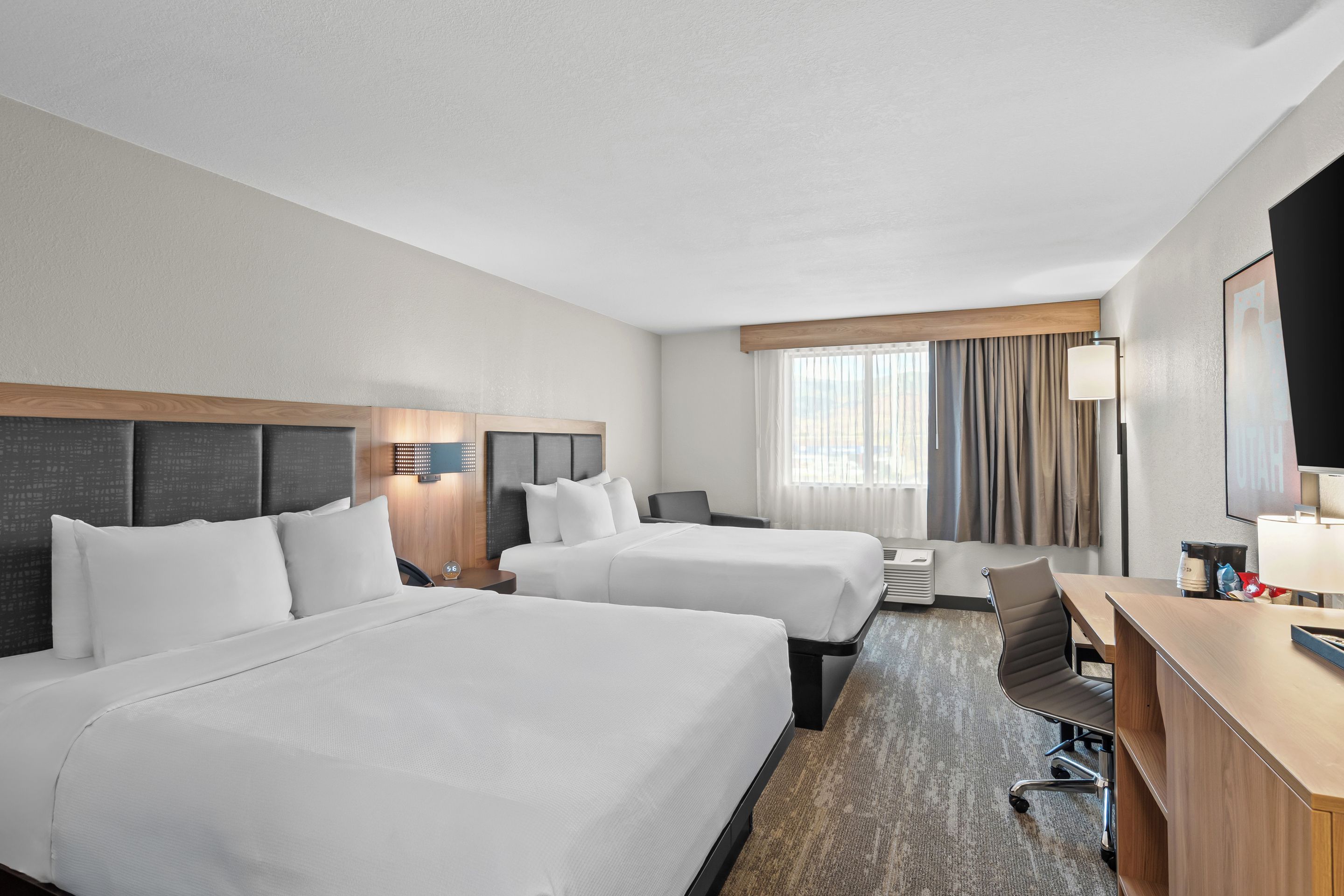 Une chambre d’hôtel avec deux lits, un bureau, une chaise, une télévision et une fenêtre avec des rideaux.