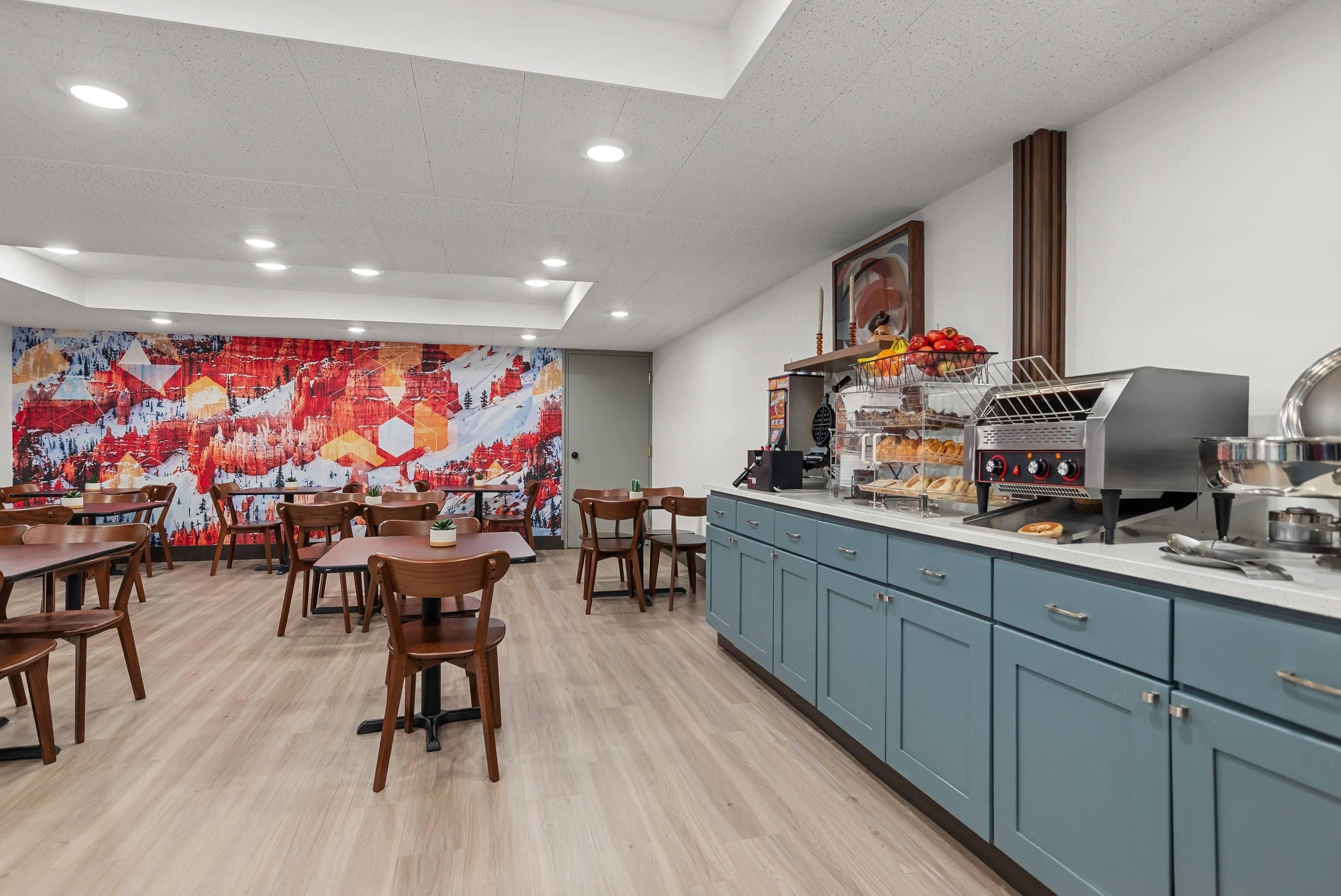 A modern kitchen with a built-in grill, a large mural, and wooden tables and chairs.