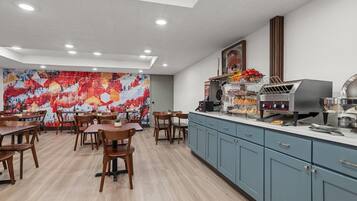 A modern kitchen with a built-in grill, a large mural, and wooden tables and chairs.
