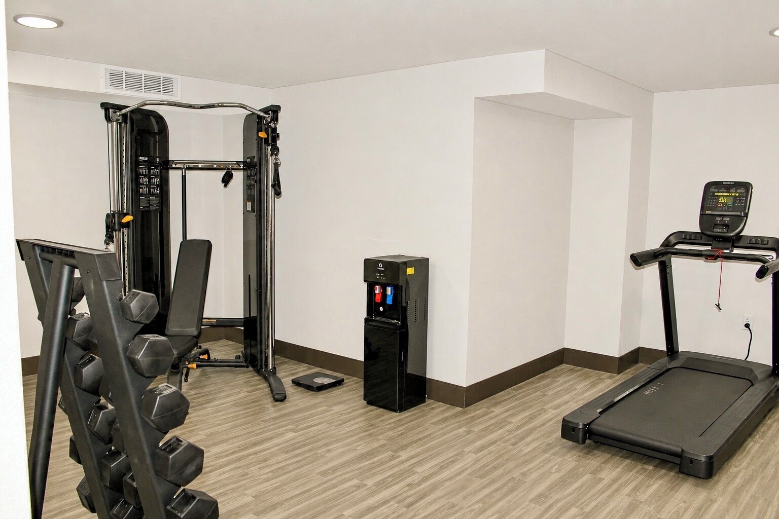 A gym with a weight machine, a treadmill, and a water dispenser.