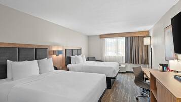 A hotel room with two beds, a desk, a chair, a TV, and a window with curtains.