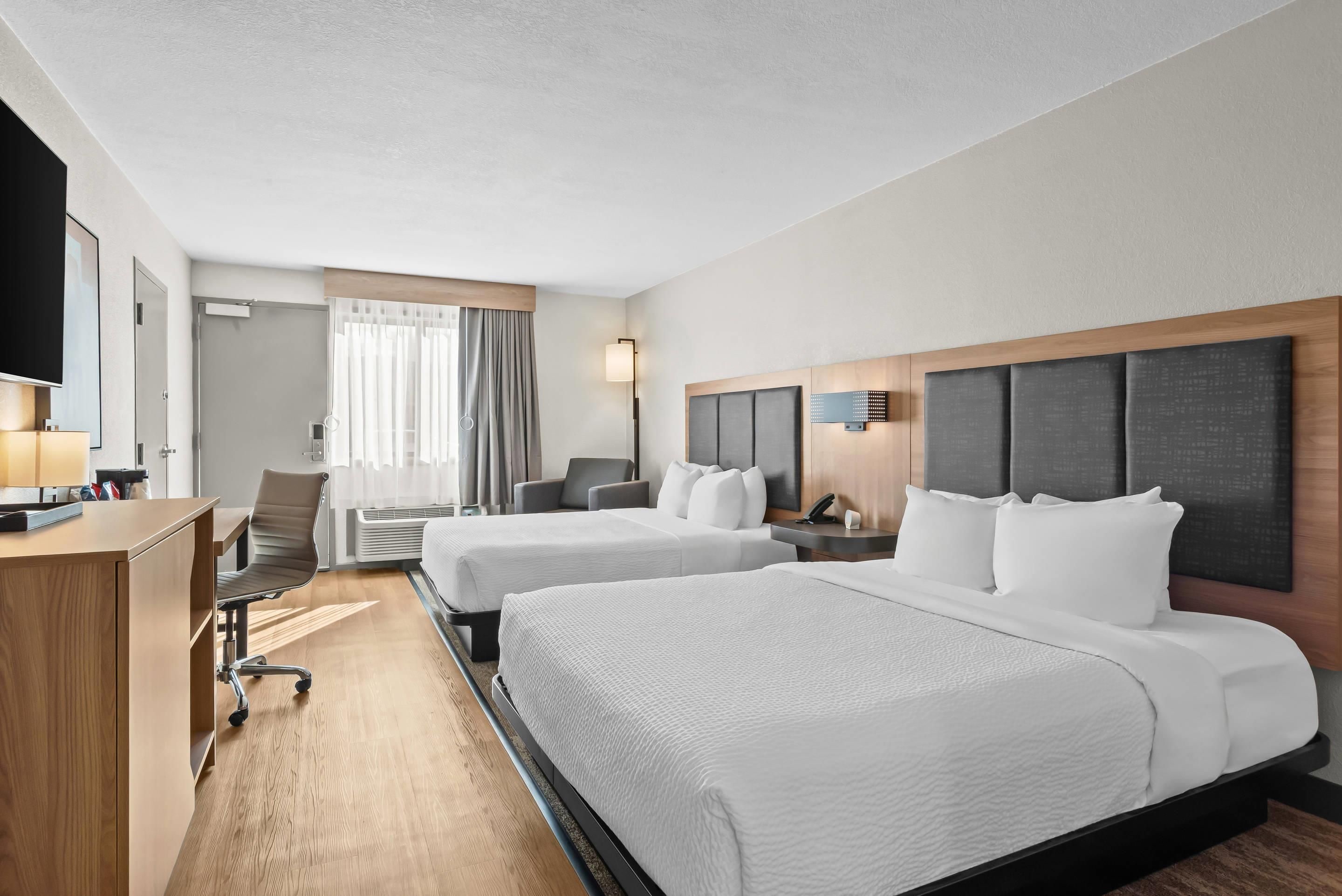A hotel room with two beds, a desk, a chair, a television, and a window with curtains.