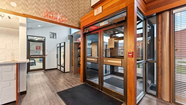 A hotel entrance with a wooden reception desk, a neon sign, and a glass door with push buttons. - The Cairn Hotel, an Ascend Collection Hotel (Cedar City)