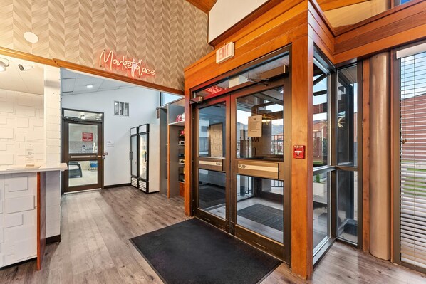 L’entrée d’un hôtel, avec un comptoir de réception en bois, une enseigne au néon et une porte en verre dotée de boutons-poussoirs.