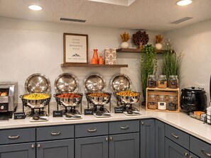 Een ontbijtbuffet met containers met duidelijke labels voor roerei, spek, worst en ontbijftaartjes.