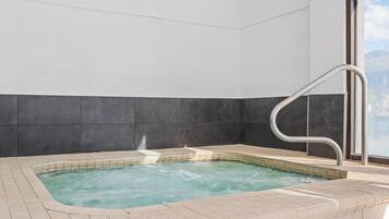 Un jacuzzi con escalera metálica, rodeado de paredes de azulejos y una ventana.